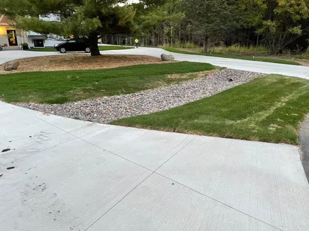Landscape design featuring a gravel drainage area and lush grass beside a concrete sidewalk.