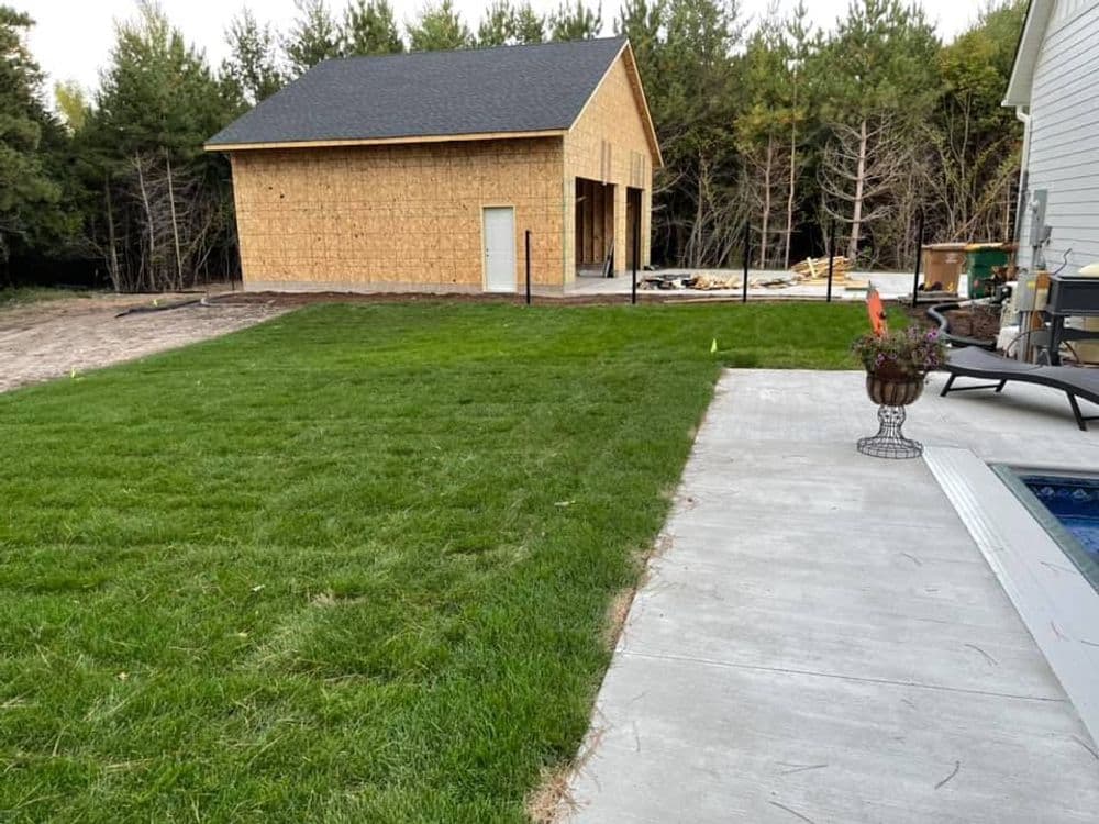 Newly constructed garage behind a lush green lawn and patio area with trees in the background.