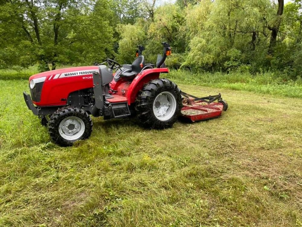 Red Massey Ferguson tractor with mower attachment in a grassy field surrounded by trees.